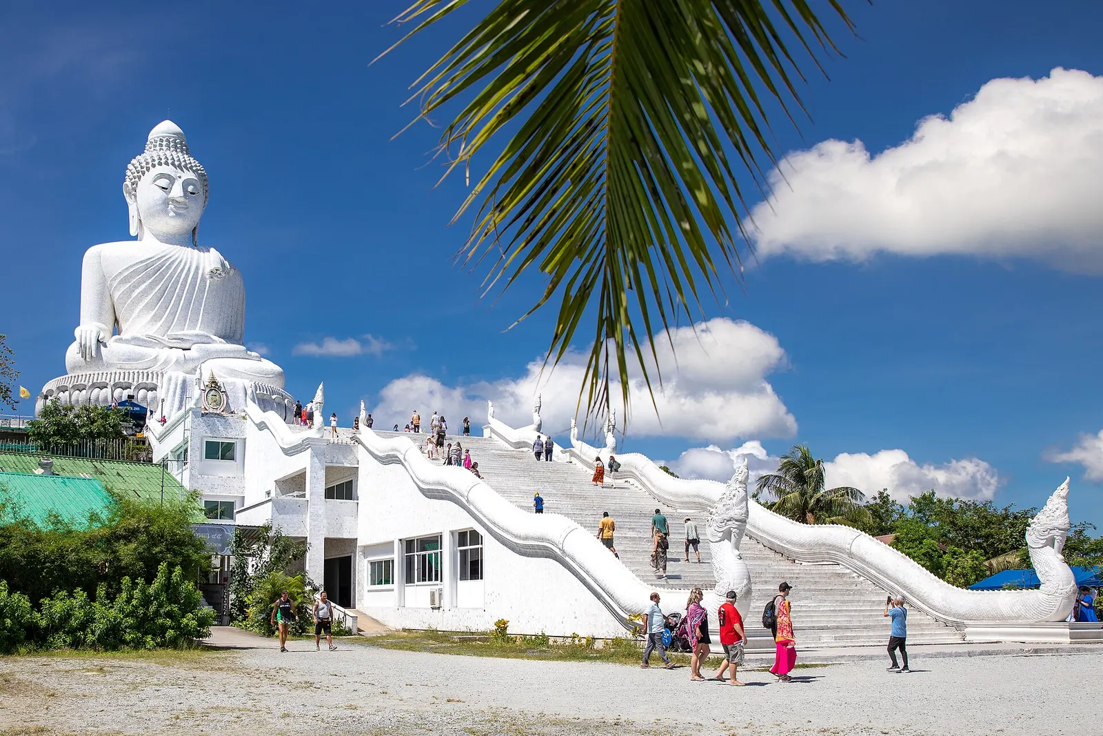 The white marble Big Buddha above Chalong, the staircase and a palm frond in the foreground