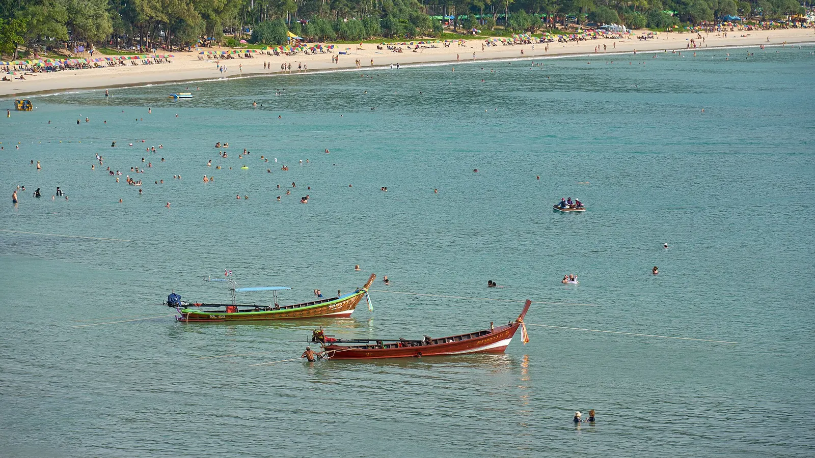 Kata Beach from above: turquoise water, swimmers and two longtail boats off the sand
