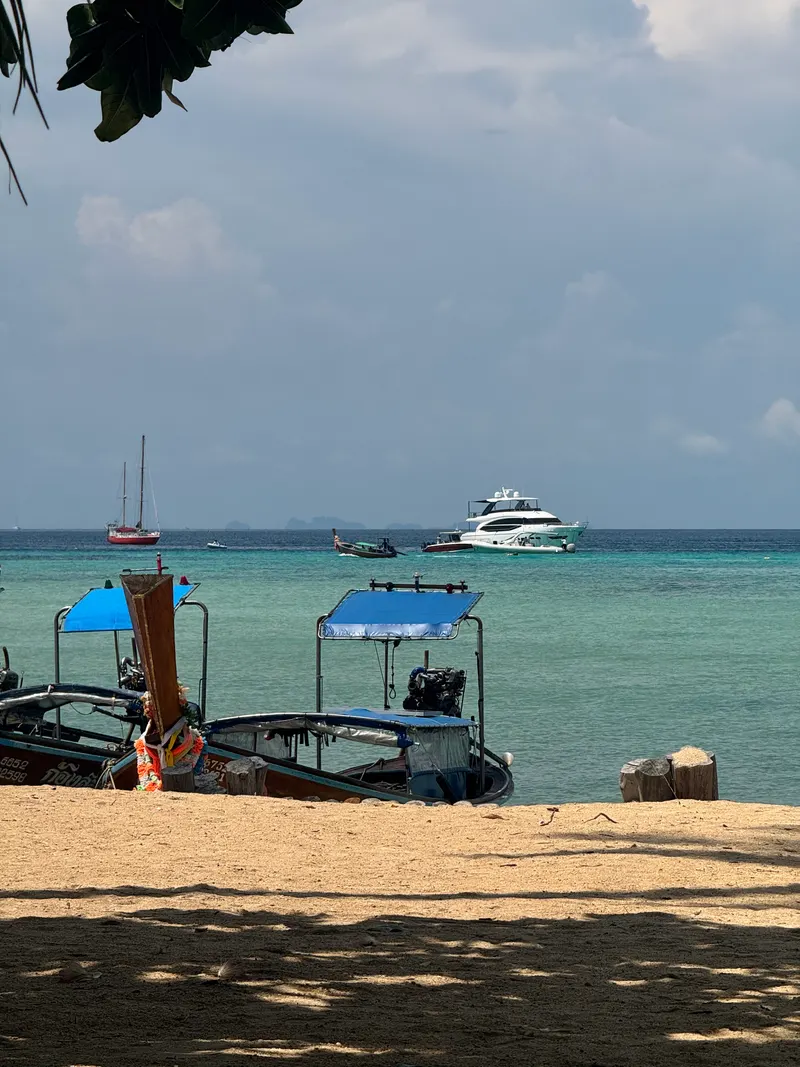 Longtail boats on the beach at Phi Phi Don, yachts anchored in the bay behind